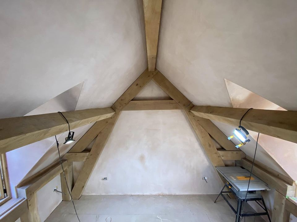 Sloped loft ceilings in fresh plaster between oak trusses