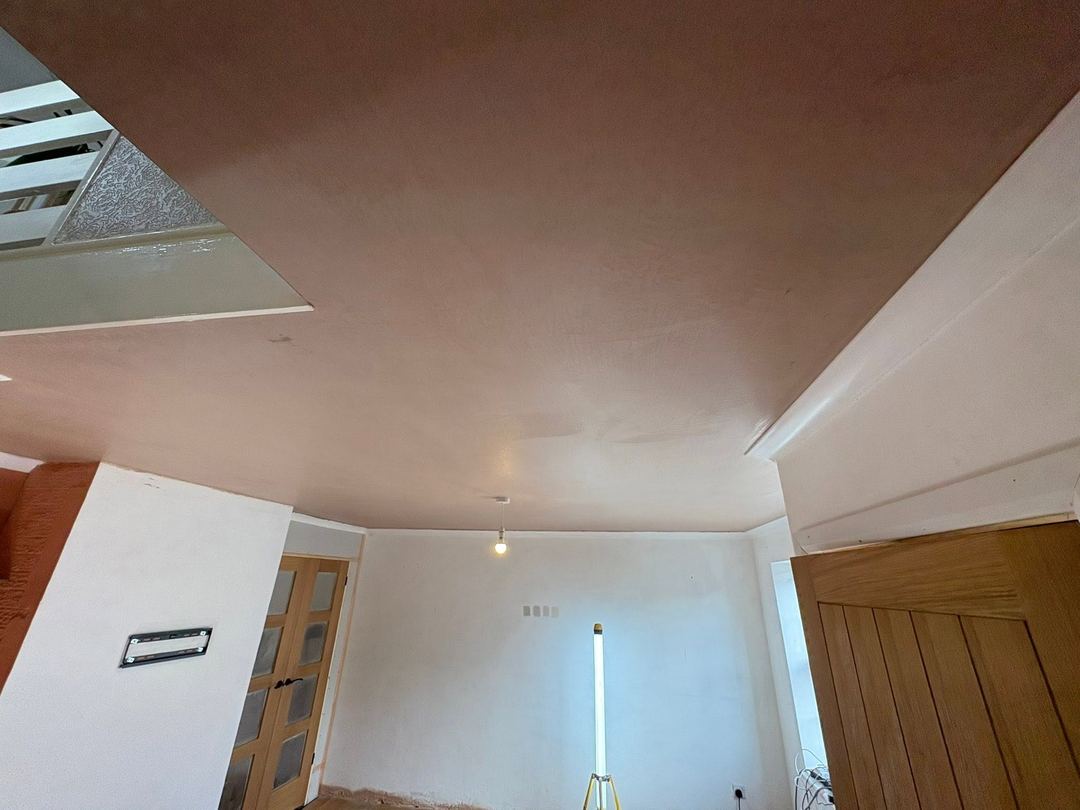 After: The same ceiling flat in fresh pink plaster, stair stringer and oak door unchanged.